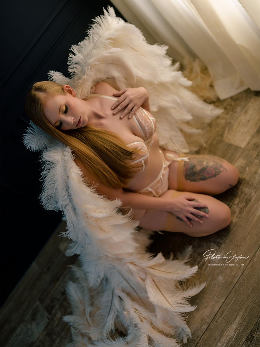 Woman kneeling on floor next to window wearing white lingerie with white angel wings